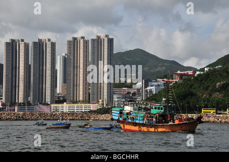 Motorised fishing junk, towing small boats, leaving the typhoon barrier at the east end of Aberdeen Harbour, Hong Kong, China Stock Photo