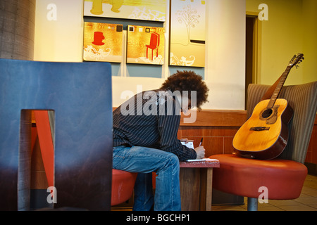 Musician at a café, writing in his journal, guitar in a chair beside him Stock Photo
