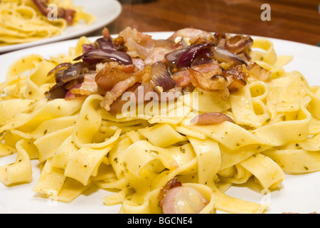 Plate of Tagliatelle pasta tossed in pesto and olive oil with fried bacon and red onion. Stock Photo