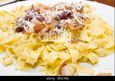 Plate of Tagliatelle pasta tossed in pesto and olive oil with fried bacon and red onion. Topped with grated parmesan cheese. Stock Photo