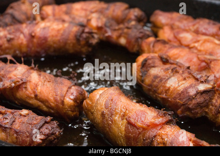 bacon wrapped sausages known in england as Piggies in Blankets, just out of the oven in roasting tin with shallow focus.