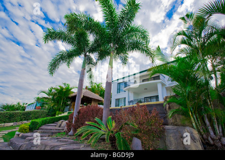 Garden with palms and Bali hut in front of waterfront mansion Stock Photo