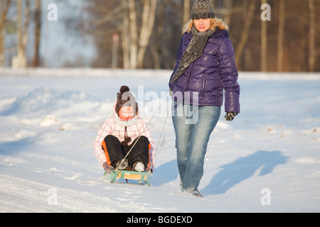 Mother pulling daughter on sledge, bright and white winter scene Stock Photo