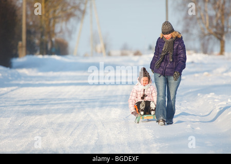 Mother pulling daughter on sledge, bright and white winter scene Stock Photo