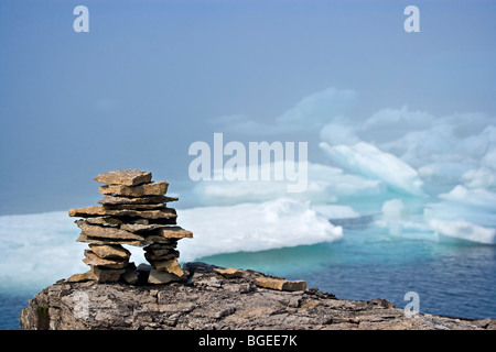 Rock inukshuk on a ledge backdropped by pack ice veiled by fog in the Strait of Belle Isle, Labrador Coastal Drive, Highway 510, Stock Photo