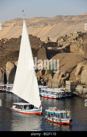 ASWAN, EGYPT. A Nile felucca and river taxi sailing past ancient ruins on Elephantine Island. 2009. Stock Photo