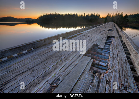 Old wooden bridge spanning the entrance to Clayoquot Arm of Kennedy Lake at sunset, a transition area of the Clayoquot Sound UNE Stock Photo