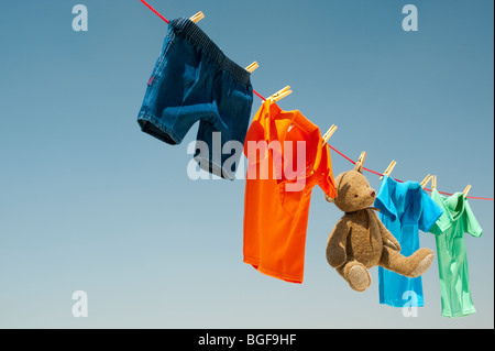 Childrens clothes and teddy bear on a washing line against a blue sky. India Stock Photo