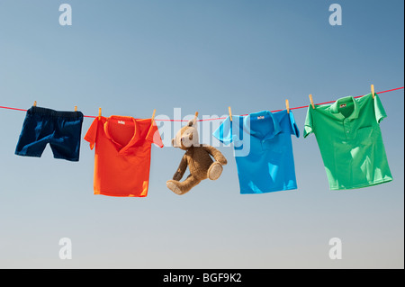 Childrens clothes and teddy bear on a washing line against a blue sky. India Stock Photo