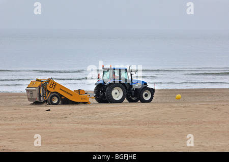Tractor-pulled beach cleaner raking sea sand at seaside resort along ...