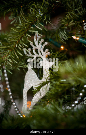 A reindeer shaped decoration hangs on a Christmas tree next to fairy lights asnd silver beads. Stock Photo