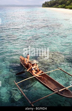 Two young woman paddling an outrigger canoe. Mentawai Islands, Sumatra, Indonesia, Southeast Asia, Asia Stock Photo