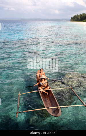Two young woman paddling an outrigger dugout canoe. Mentawai Islands, Sumatra, Indonesia, Southeast Asia, Asia Stock Photo