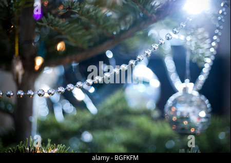 A length of silver decorative beading is draped on a pine Christmas tree, with a collection of other decorations behind. Stock Photo