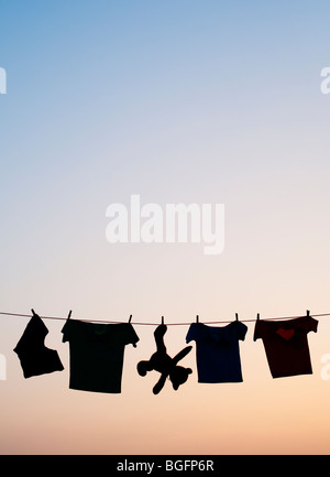 Childrens clothes and teddy bear on a washing line silhouette at dawn. India Stock Photo