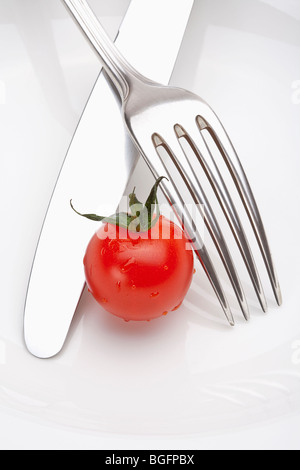 cherry tomato on a plate with fork and knife isolated on white Stock Photo