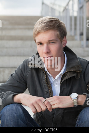 Young blond handsome chap sitting on the stairs outdoors Stock Photo