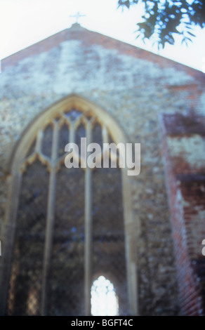Impressionistic view of chancel east window and flint wall with brick buttress of English Gothic church with ash tree Stock Photo
