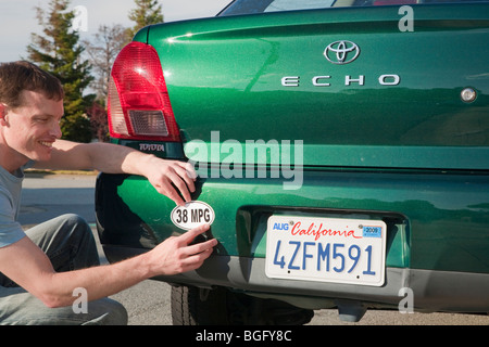 Man placing a 38 miles per gallon fuel efficiency bumper sticker installed on Toyota Echo car. California, USA Stock Photo