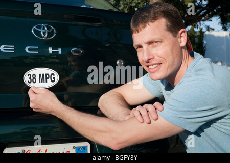 Mid adult man placing a 38 miles per gallon fuel efficiency bumper sticker installed on Toyota Echo car. Stock Photo