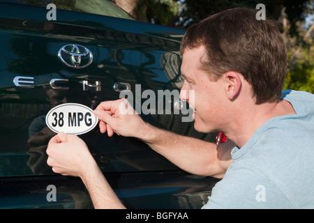 Mid adult man placing a 38 miles per gallon fuel efficiency bumper sticker installed on Toyota Echo car. California, USA Stock Photo