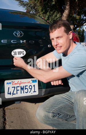 Mid adult man placing a 38 miles per gallon fuel efficiency bumper sticker installed on Toyota Echo car. Stock Photo