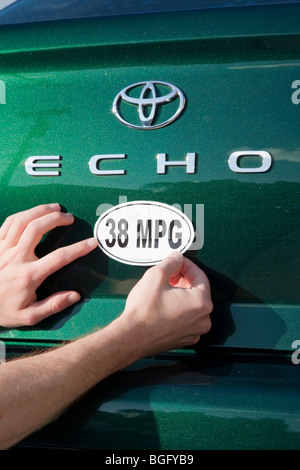 Man placing a 38 miles per gallon fuel efficiency bumper sticker installed on Toyota Echo car. California, USA Stock Photo