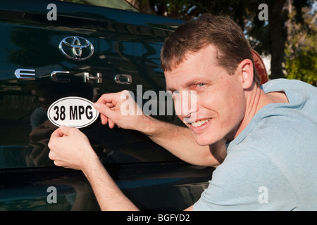 Mid adult man placing a 38 miles per gallon fuel efficiency bumper sticker installed on Toyota Echo car. California, USA Stock Photo