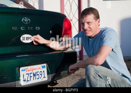 Mid adult man placing a 38 miles per gallon fuel efficiency bumper sticker installed on Toyota Echo car. California, USA Stock Photo