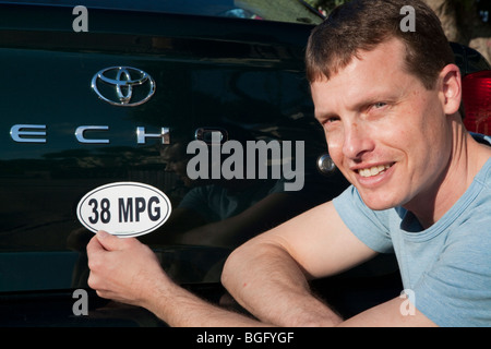 Mid adult man placing a 38 miles per gallon fuel efficiency bumper sticker installed on Toyota Echo car. Stock Photo