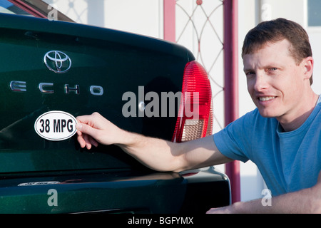 Mid adult man placing a 38 miles per gallon fuel efficiency bumper sticker installed on Toyota Echo car. California, USA Stock Photo