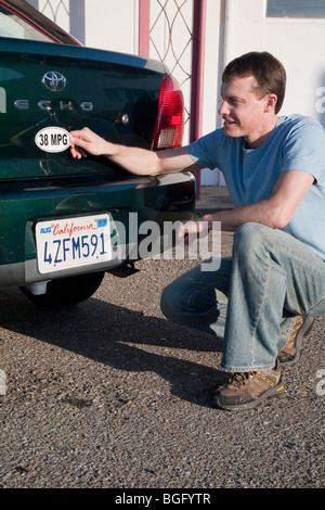 Mid adult man placing a 38 miles per gallon fuel efficiency bumper sticker installed on Toyota Echo car. California, USA Stock Photo