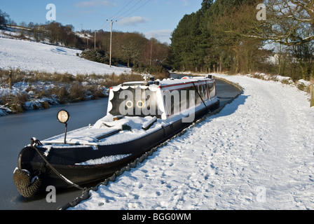 moored black narrow boat along peak forest canal covered in snow Stock Photo