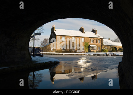 framed view under bridge at peak forest macclesfield canal intersection of canal side stone cottages in the snow Stock Photo