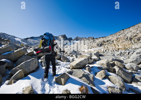 A woman wearing a backpack hiking in the snow through some high alpine landscape, Enchantment Lakes Wilderness Area Stock Photo