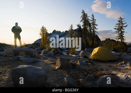 A silhouetted man watching the sun rise over his camp site in the Upper Enchantments, Cascade Range, Washington, USA. Stock Photo