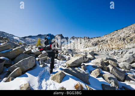 A woman wearing a backpack hiking in the snow through some high alpine landscape, Enchantment Lakes Wilderness Area, Stock Photo