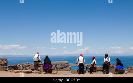 Men & Women of Taquile Island sitting on wall in traditional clothes overlooking Lake Titicaca Stock Photo