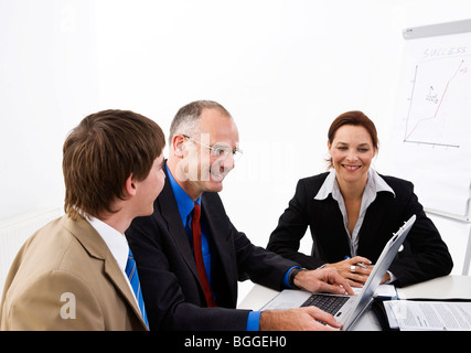 Business people sitting at a table, looking at a laptop Stock Photo