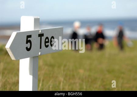 Sign to the 5th tee at golf course with four golfers walking in background blurred. Stock Photo