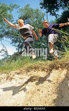 two young boys jumping off a sand dune together Stock Photo