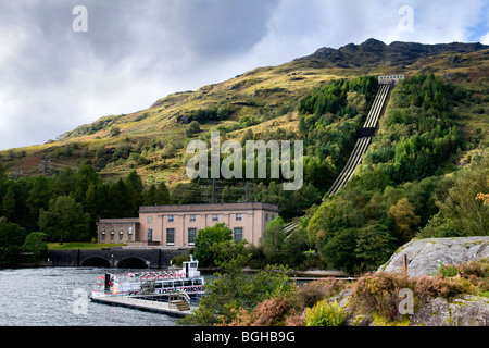 Loch Sloy hydro electric power station tunnels down Ben Vorlich onto shores of Loch Lomond with cruise boat in foreground Stock Photo