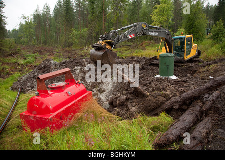 Movable above ground diesel fuel tank , digger digging sewer pipeline with waste storage well and pumping station at forest , Finland Stock Photo