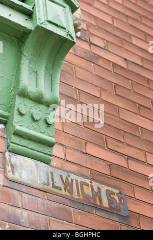 An old rusted street sign on a red brick wall, with the corner of a green window casing, that looks to have been painted over. Stock Photo