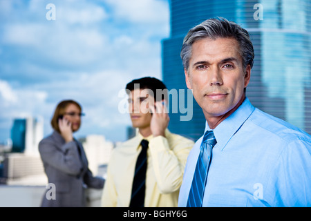 An older grey-haired businessman and his team on mobile phones in a downtown setting. Stock Photo
