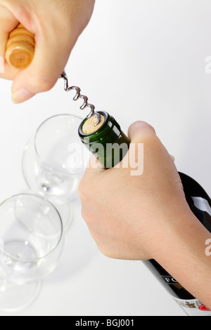 A woman's hands opening a bottle of wine with a corkscrew. Two empty wine glasses are in the background Stock Photo