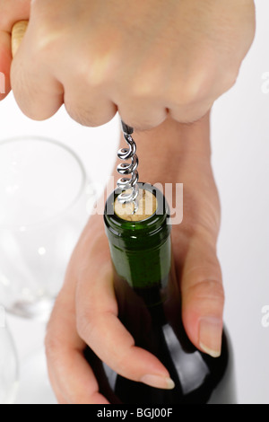 A woman's hands opening a bottle of wine with a corkscrew. An empty wine glass is in the background Stock Photo