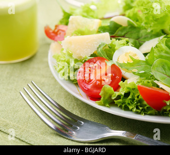 Fresh salad with tomato and quail eggs in a white bowl on a green tablecloth