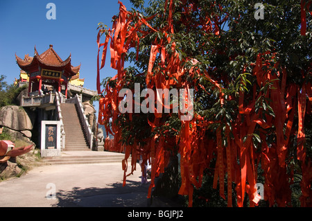 Red prayer ribbons in a tree near a Buddhist pavilion on Jiuhua Shan. Anhui province, China. Stock Photo