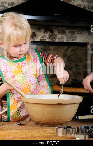 Stock photo of a four year old girl using a wooden spoon to mix up some cookie dough to make biscuits. Stock Photo